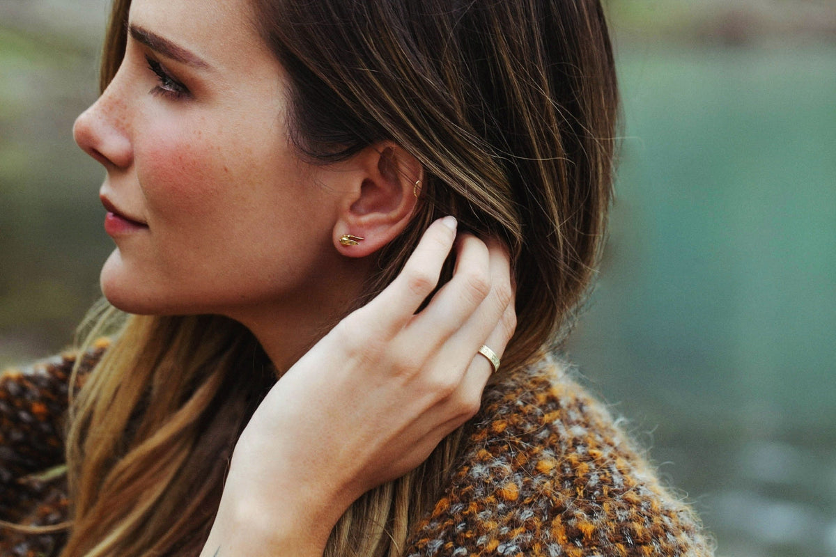 Profile view of a woman wearing Officially Licensed Harry Potter fine jewelry by Freeman Design on a blurred background. Jewelry featured: Golden Pearl Snitch Earrings in solid 14k yellow gold. Also available in solid 18k yellow gold. 