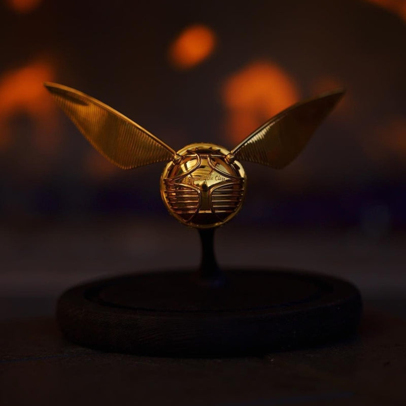 Officially licensed Harry Potter Golden Snitch Ring box in 14k yellow gold resting on its stand over a blurred background. Also available in gold plated sterling silver and platinum. 