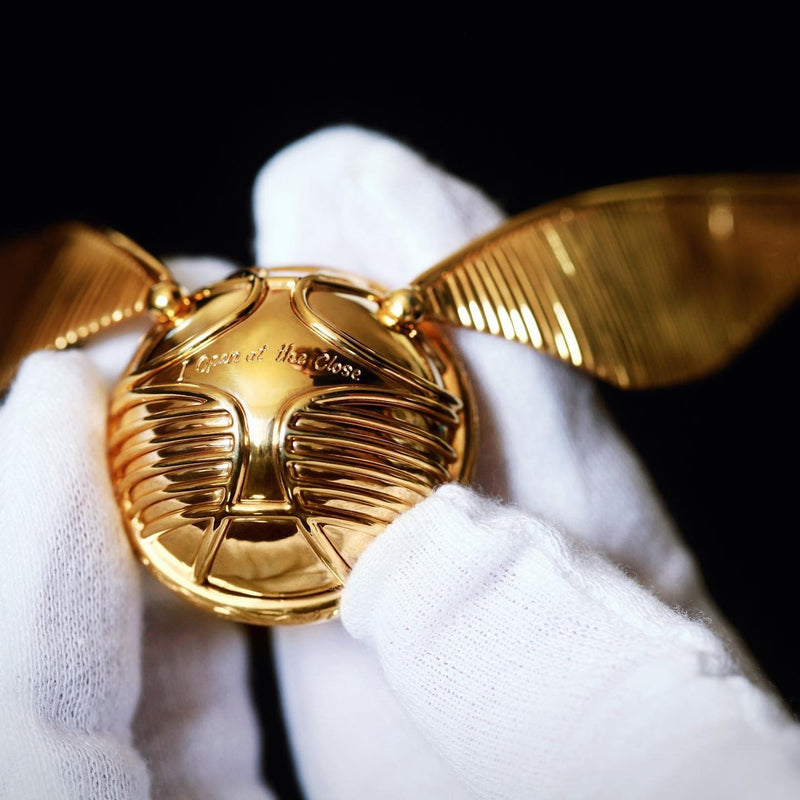 Close top view of officially licensed Harry Potter Golden Snitch Ring box in solid 14k yellow gold in a white gloved hand. Inscription on ring box reads, “I Open at the Close.” Also available in gold plated sterling silver and platinum. 